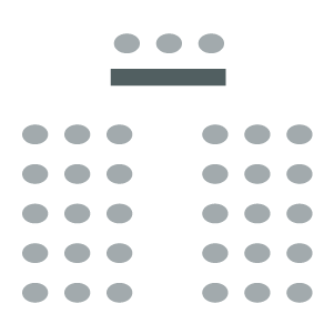 Room set up with rows of chairs with central aisle facing speaker table and chairs at front of room.