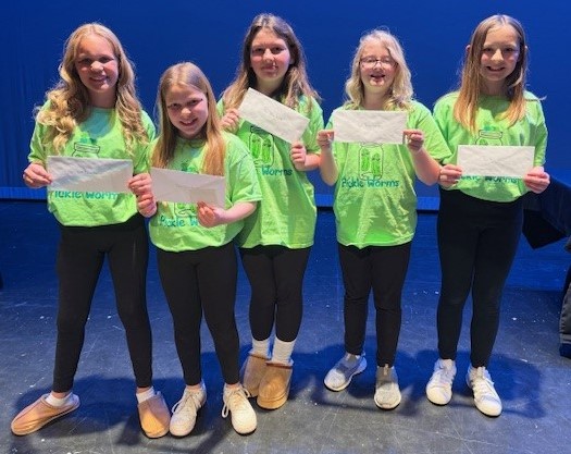 Five girls in green shirts and black pants holding the award envelope for Best Team Name: Pickle Worms