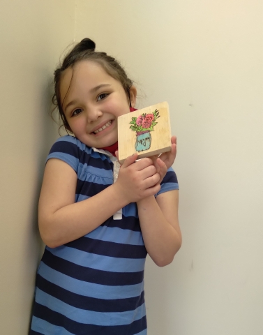 Girl in blue striped dress holding wooden block with a vase and flowers on it