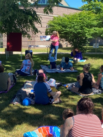 People sitting outside on blankets listening to the librarian read a book.