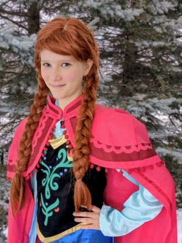 Girl with red braids and a pink cape and embroidered black and blue dress