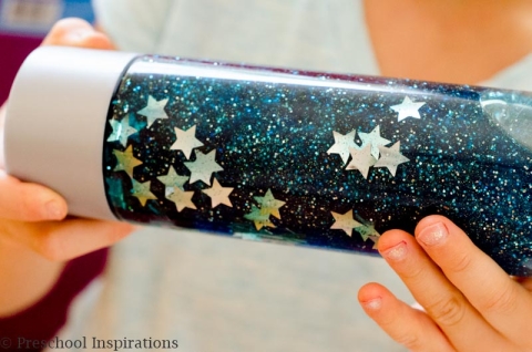 Hands holding a bottle with blue shimmering liquid and white stars in it.