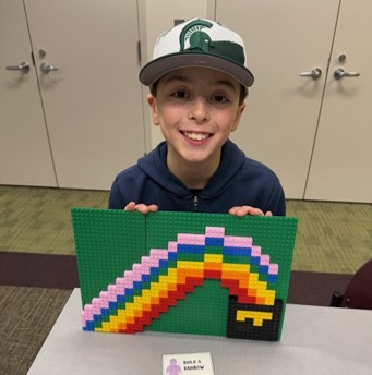 Boy with baseball cap smiling holding a Lego creation of a rainbow
