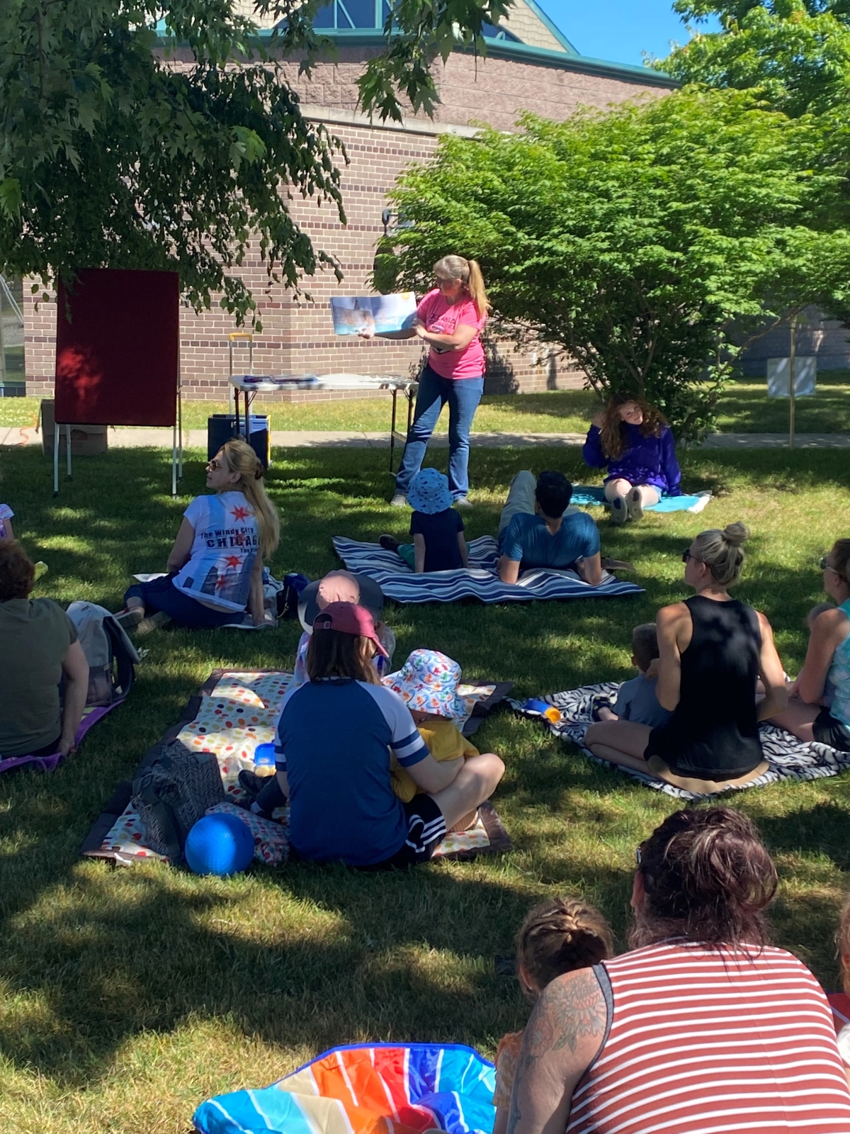 People sitting outside on blankets listening to the librarian read a book.