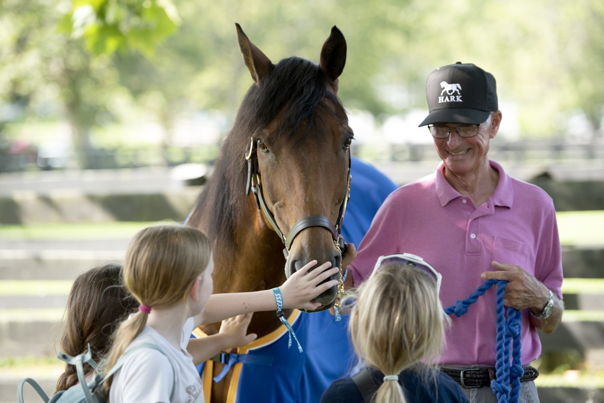 Brown horse surrounded by 3 children petting its nose and and older man holding the reins.